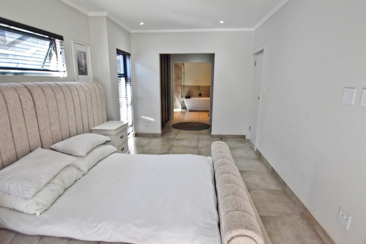Spacious bedroom featuring neutral tiled flooring, recessed lighting, and direct access to an en-suite bathroom with a modern layout.