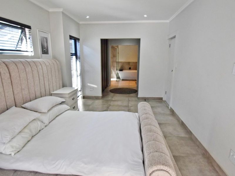 Spacious bedroom featuring neutral tiled flooring, recessed lighting, and direct access to an en-suite bathroom with a modern layout.