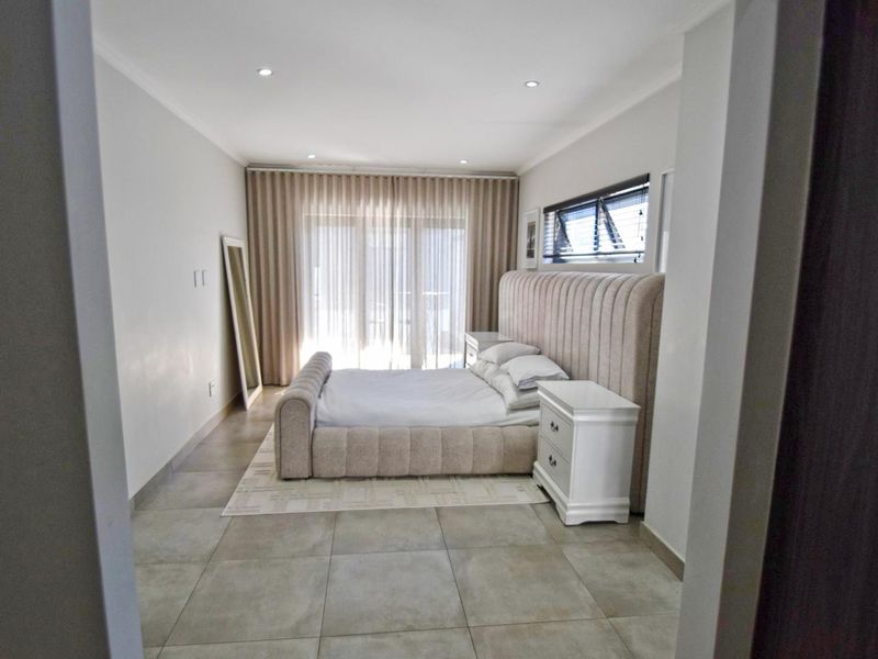 A well-maintained bedroom featuring large format floor tiles, recessed lighting, and a sliding glass door leading to an outdoor area.