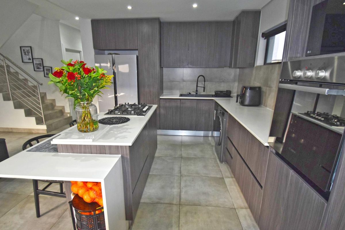 Modern kitchen featuring dark wood cabinetry, stone countertops, a central island with a gas hob, and integrated appliances with tiled flooring.