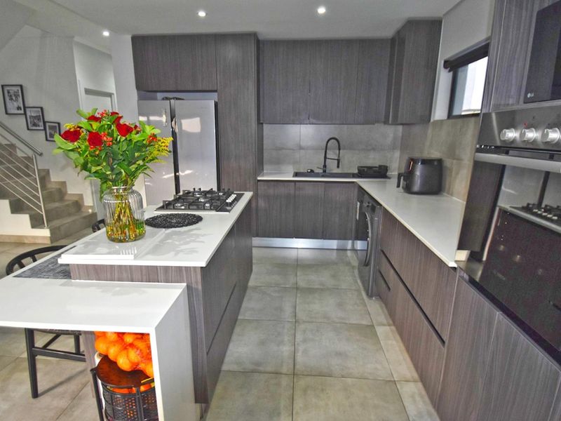 Modern kitchen featuring dark wood cabinetry, stone countertops, a central island with a gas hob, and integrated appliances with tiled flooring.