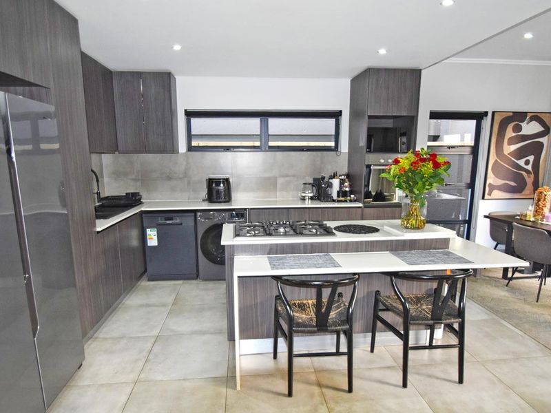 Modern open-plan kitchen featuring dark wood cabinetry, stone countertops, a central island with breakfast bar, and integrated gas cooktop and oven.
