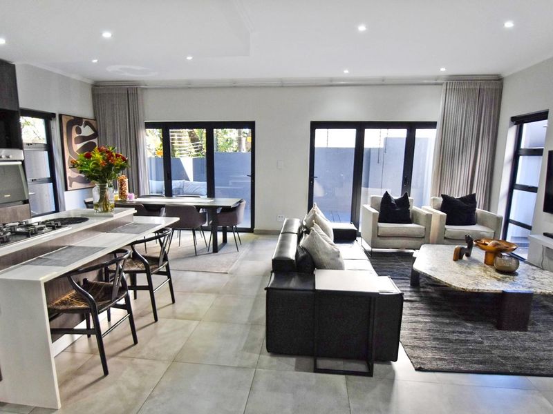 Modern open-plan living area featuring a sleek kitchen with island, gas hob, and seamless flow to the outdoor patio through large sliding glass doors.