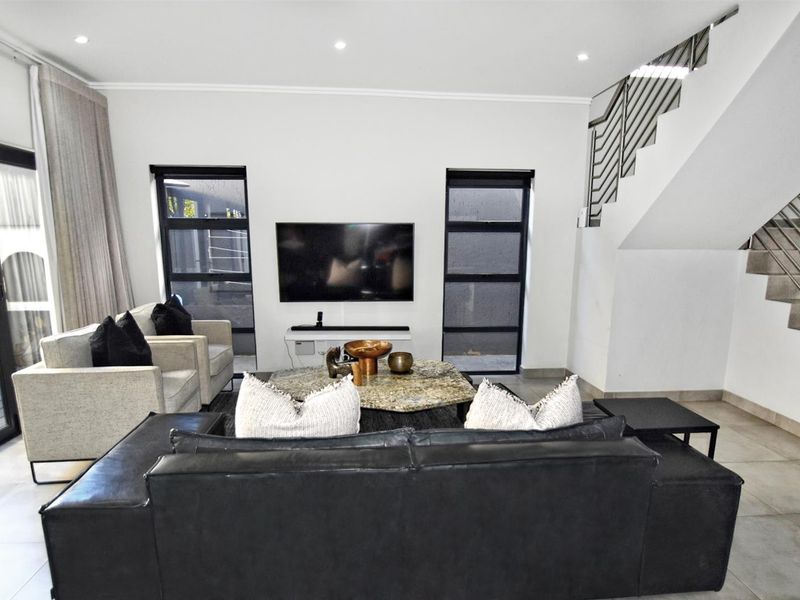 Modern living room featuring tiled flooring, recessed lighting, and a staircase with a contemporary metal balustrade, leading to an outdoor patio area.
