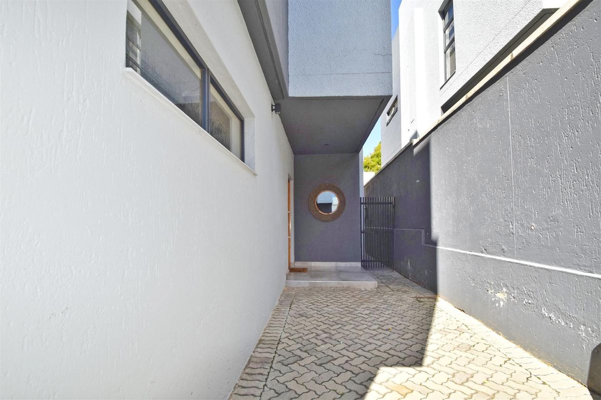 A side walkway featuring paved flooring, a metal security gate, and a recessed entrance area with modern grey exterior wall finishes.