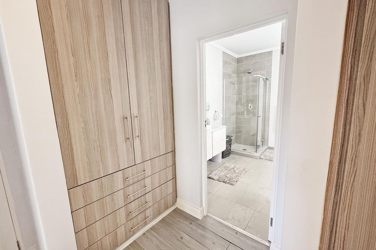 A modern bathroom featuring a glass-enclosed shower, vanity basin, and adjacent built-in cabinetry with wood-grain finish.