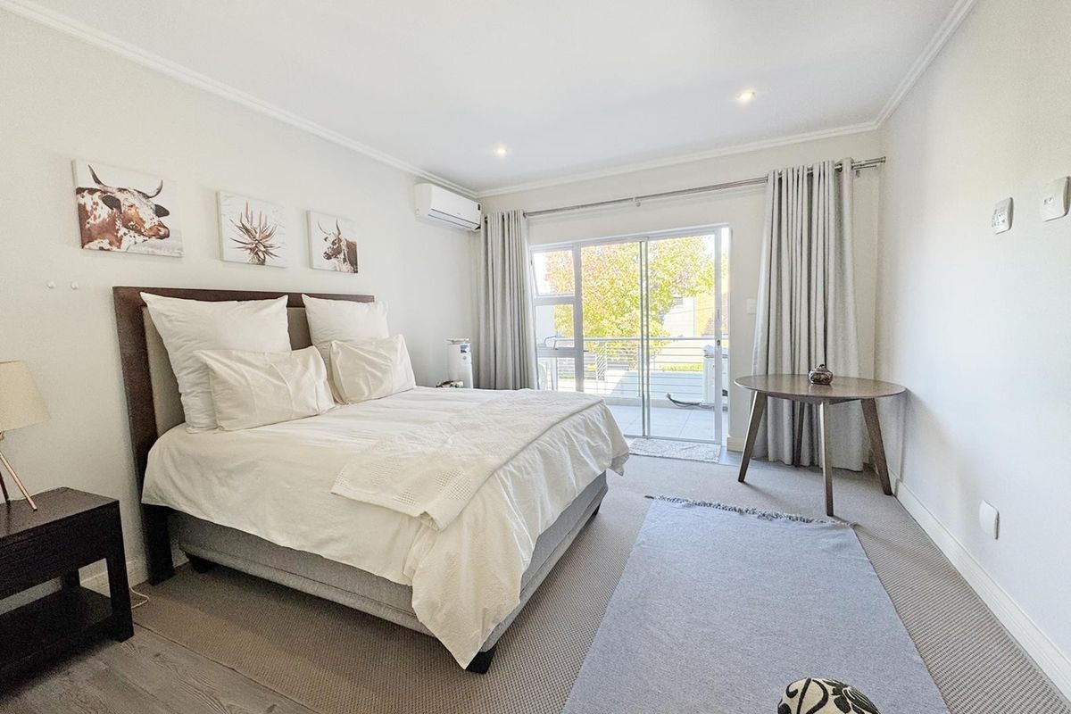 A bright and well-maintained bedroom featuring neutral tones, recessed lighting, an air conditioning unit, and direct access to a private balcony through sliding glass doors.