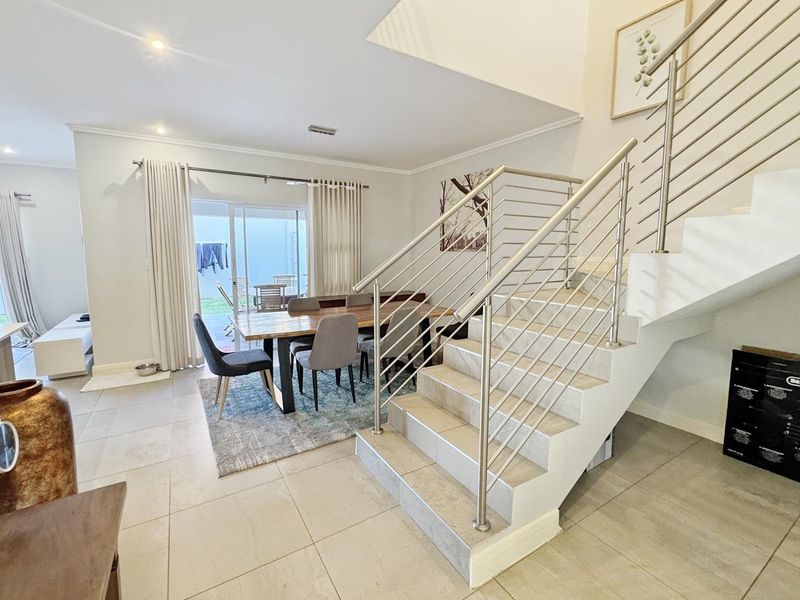 Open-plan living and dining area featuring tiled floors, a modern staircase with stainless steel balustrades, and direct access to the rear patio.