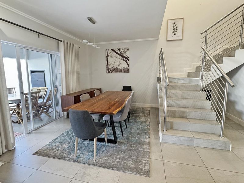 Bright dining area featuring tiled floors, a modern staircase with stainless steel railings, and large sliding doors providing access to the outdoor patio.