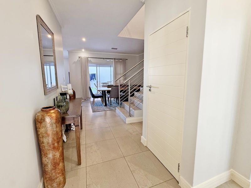 A bright entrance hall featuring tiled flooring and a modern staircase with a stainless steel balustrade, leading into the open-plan living area.
