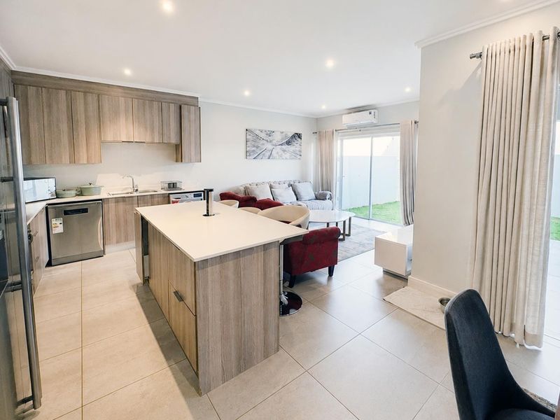 Modern open-plan living area featuring a contemporary kitchen with island, tiled floors, and seamless flow to the outdoor patio through sliding glass doors.