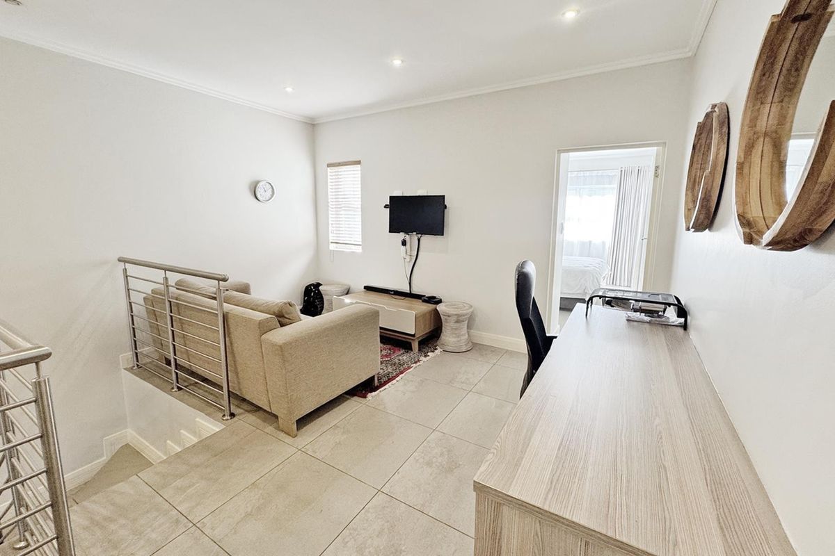 A bright living area featuring tiled flooring, recessed downlighting, and a modern stainless steel balustrade overlooking the staircase.