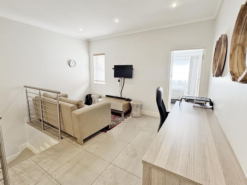 A bright living area featuring tiled flooring, recessed downlighting, and a modern stainless steel balustrade overlooking the staircase.
