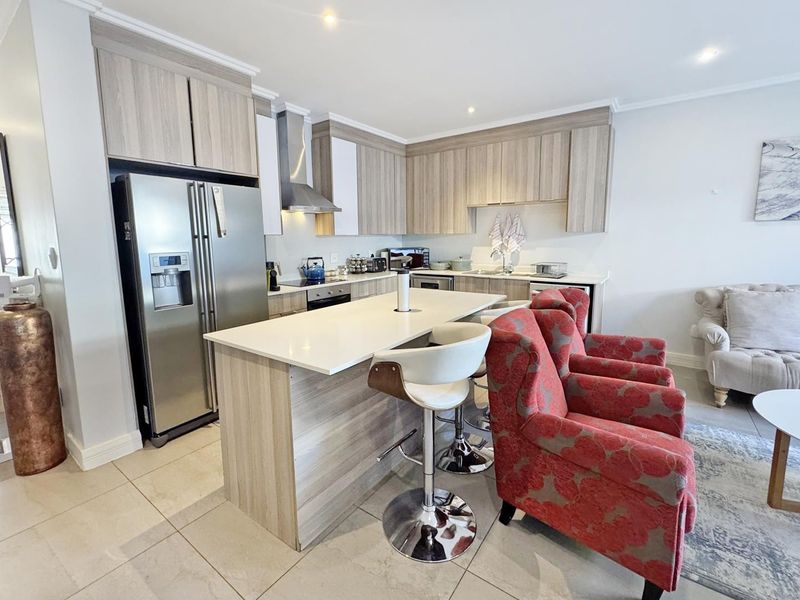 Modern open-plan kitchen featuring light wood-grain cabinetry, a central island with breakfast bar, and integrated appliances, seamlessly flowing into the living area.