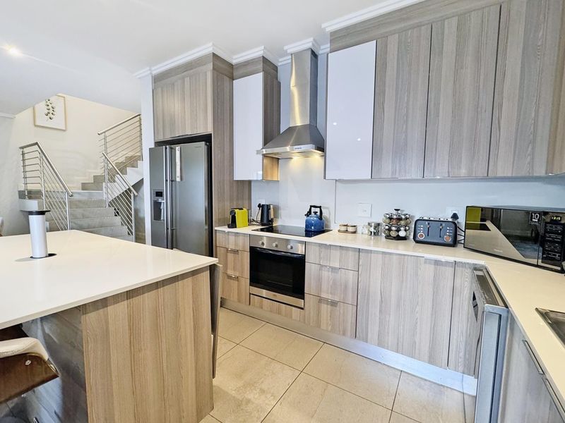 Modern kitchen featuring wood-grain cabinetry, stone countertops, a central island, and integrated stainless steel appliances, adjacent to an open staircase.