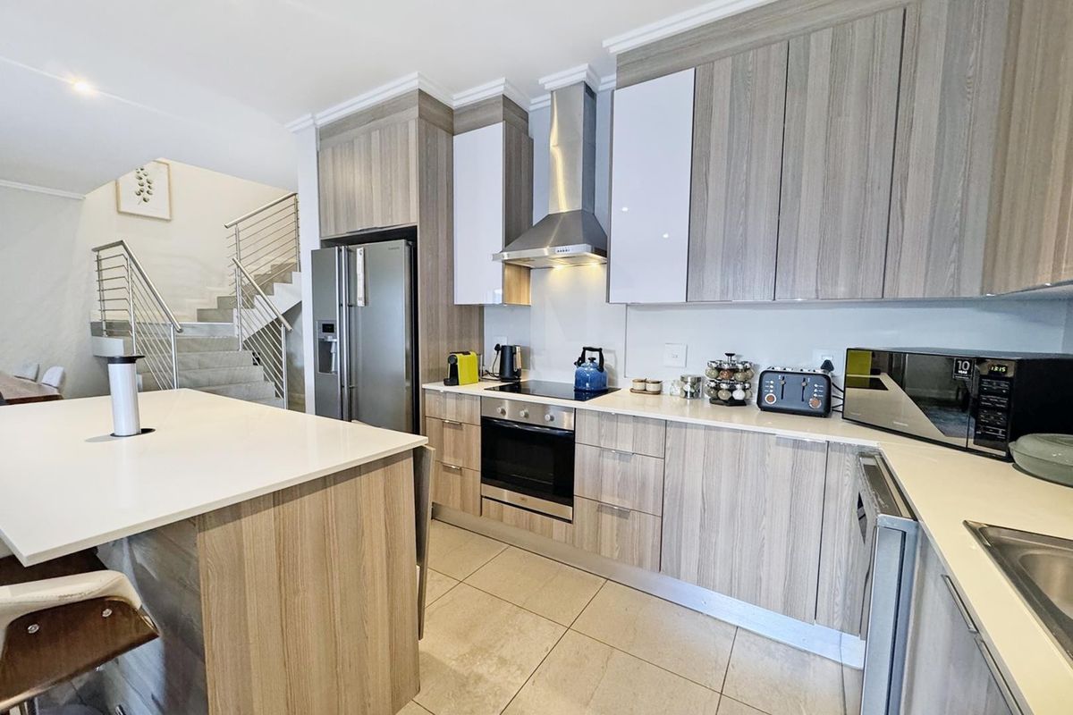 Modern kitchen featuring wood-grain cabinetry, stone countertops, a central island, and integrated stainless steel appliances, adjacent to an open staircase.