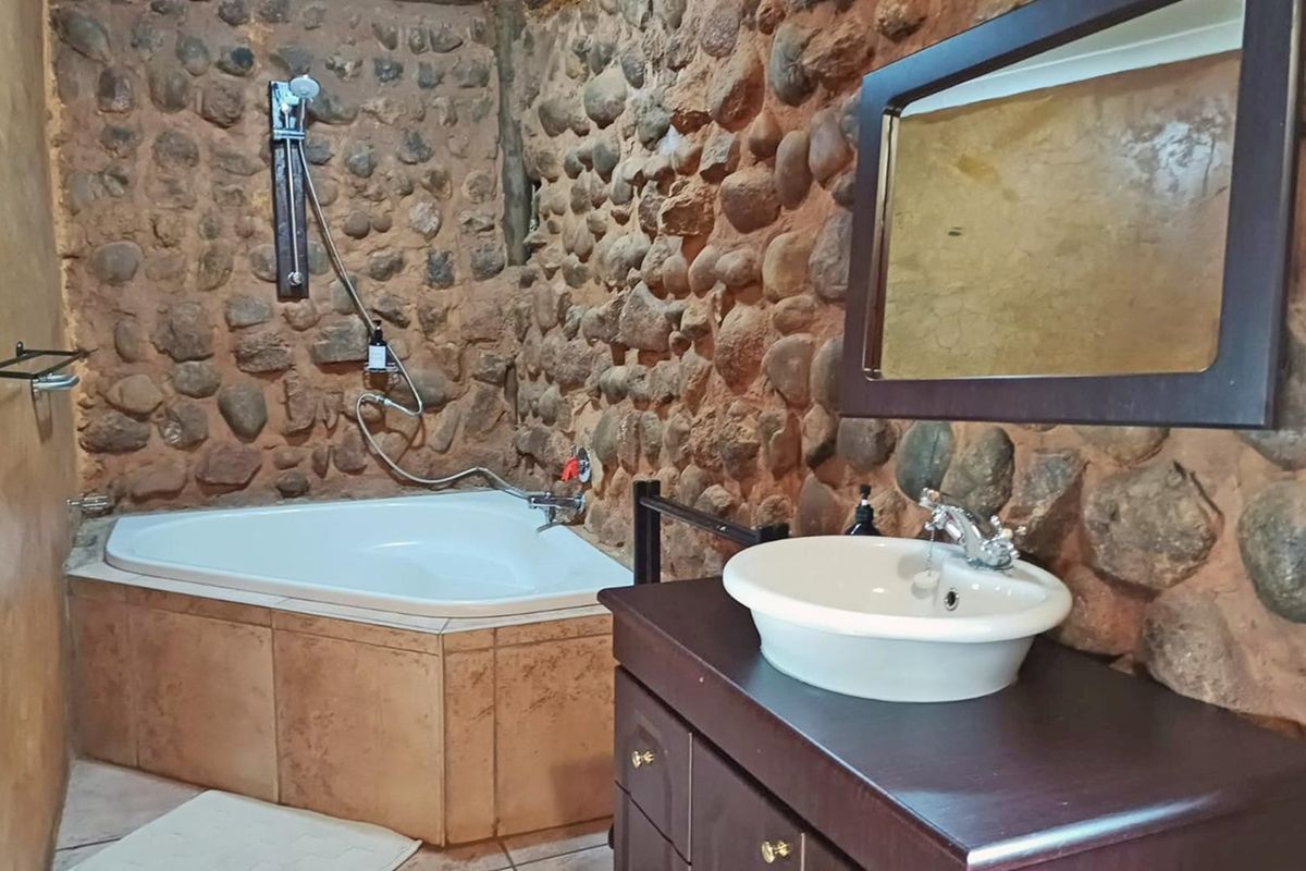 A rustic bathroom featuring unique stone-clad walls, a corner bathtub with shower attachment, and a dark wood vanity with a vessel sink.