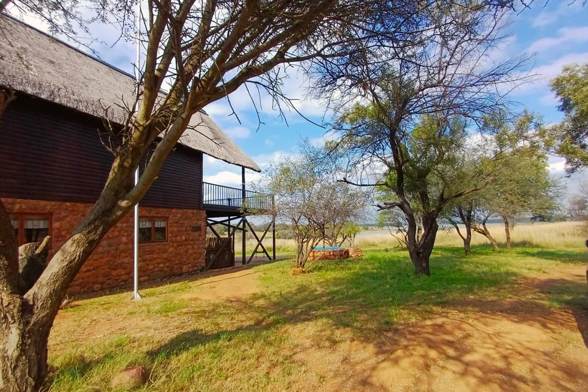 Rear view of a rustic house featuring stone cladding, a thatched roof, and an elevated timber balcony overlooking a natural landscape.