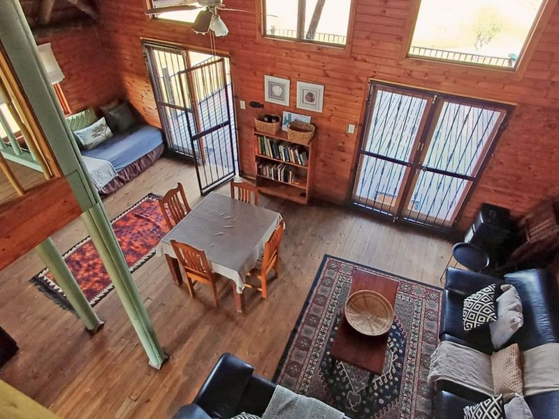 Open-plan living and dining area featuring warm timber wall cladding, wooden flooring, exposed beams, and a mezzanine level with access to outdoor security gates.