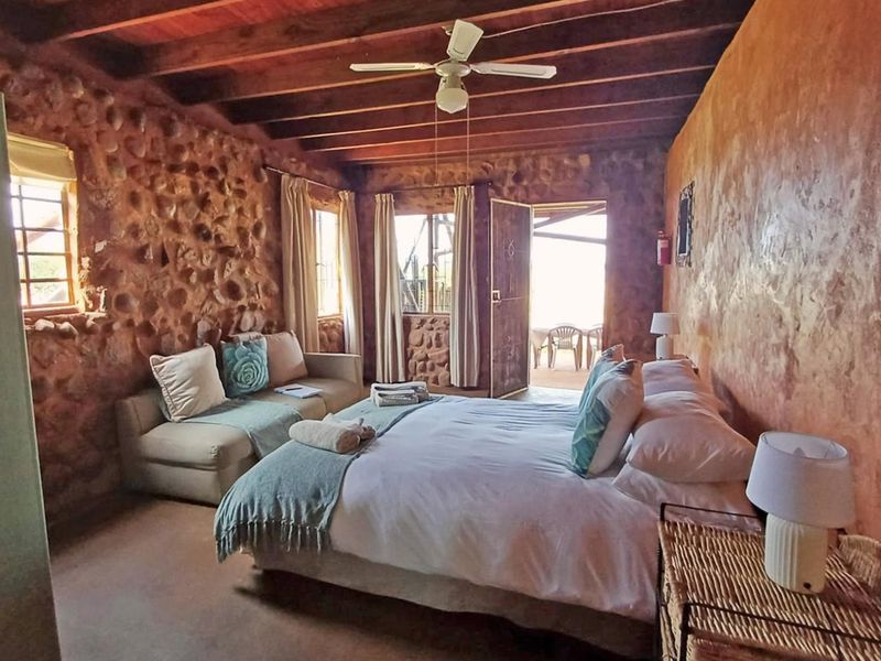 Rustic bedroom featuring exposed timber beam ceilings, textured stone masonry walls, and direct access to an outdoor patio area.