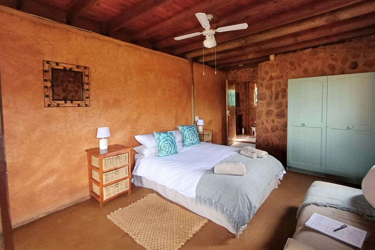 Rustic bedroom featuring exposed timber beam ceilings, textured plaster walls, a stone feature wall, and a built-in wardrobe.