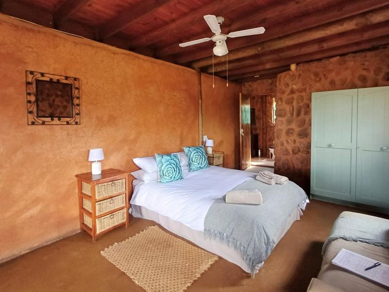 Rustic bedroom featuring exposed timber beam ceilings, textured plaster walls, a stone feature wall, and a built-in wardrobe.