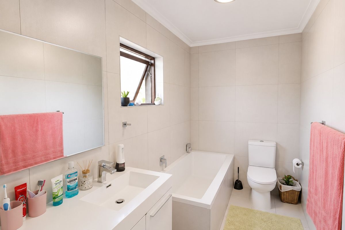 A modern, well-maintained bathroom featuring neutral wall tiles, a built-in vanity with basin, a bathtub, and a toilet.