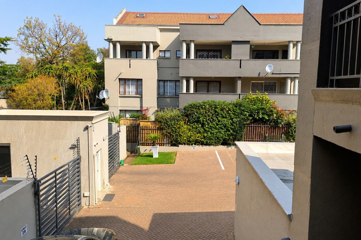 View of the apartment complex rear exterior, featuring a paved driveway, secure gated access, electric fencing, and multi-level balconies.