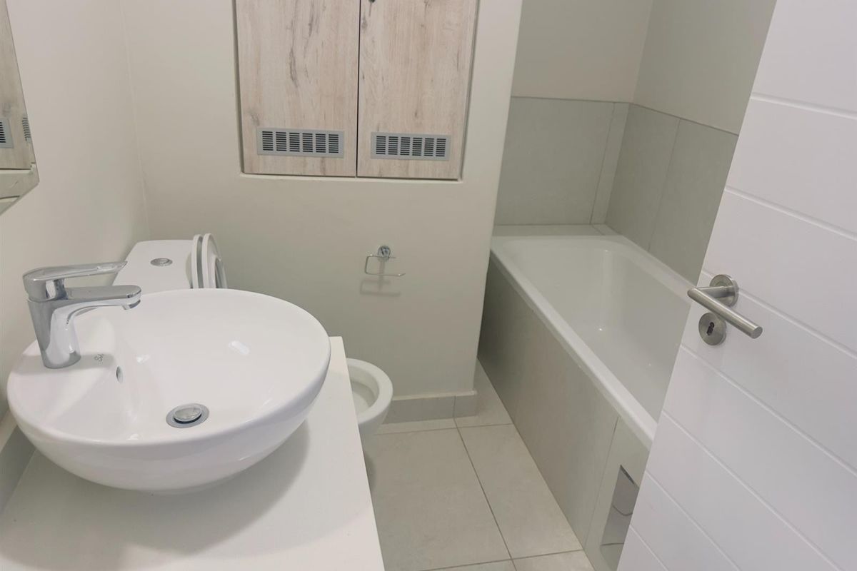 A clean, modern bathroom featuring a white vessel sink, chrome faucet, and a built-in bathtub with neutral floor tiling.