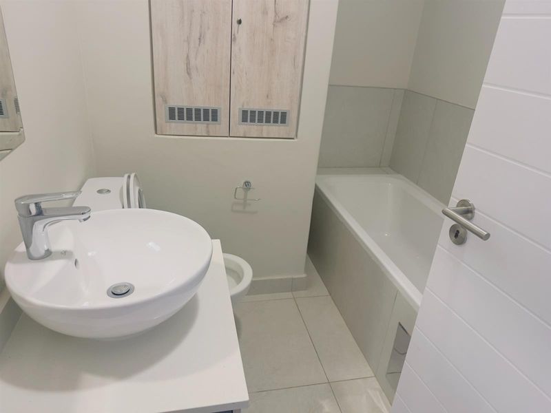 A clean, modern bathroom featuring a white vessel sink, chrome faucet, and a built-in bathtub with neutral floor tiling.
