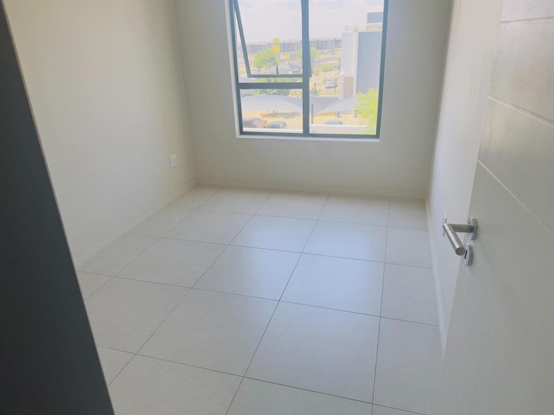 A bright, empty bedroom featuring neutral tiled flooring and a large aluminium-framed window, offering a clean and modern blank canvas.