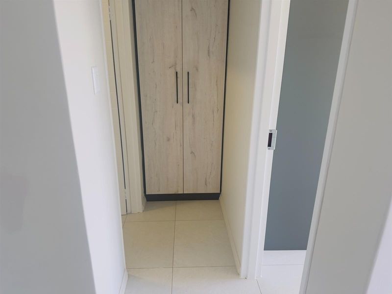 A clean, modern hallway featuring light-toned tiled flooring and a built-in storage cupboard with wood-grain finish.