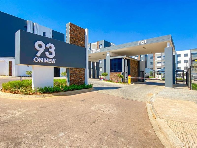 Modern apartment complex entrance featuring a secure gatehouse, boom gate access, and contemporary stone-clad signage.