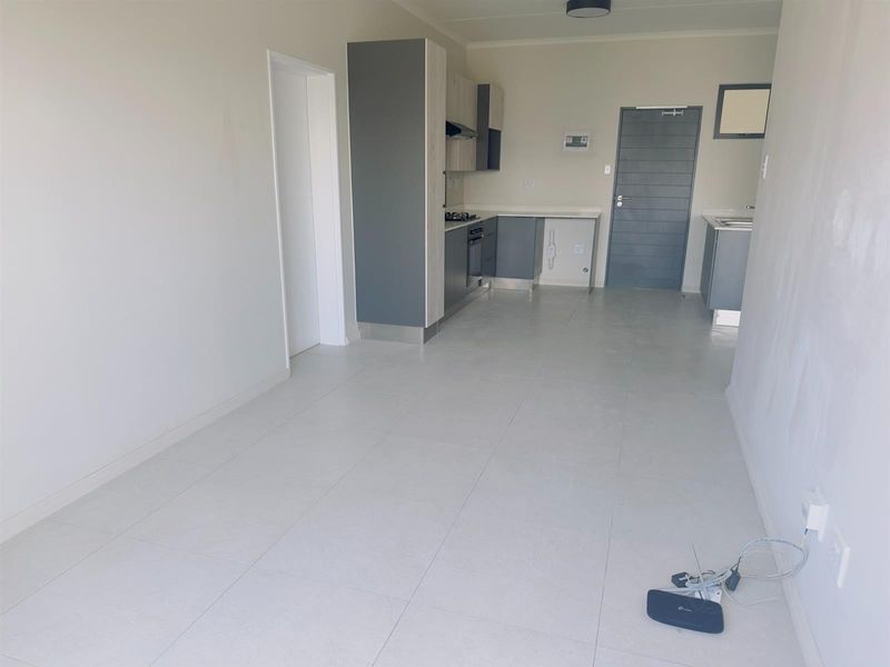 An open-plan living and kitchen area featuring modern grey cabinetry, built-in appliances, and neutral tiled flooring in a clean, vacant space.