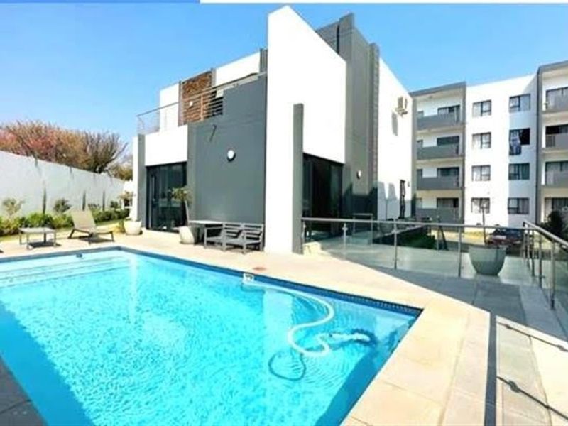 A modern apartment complex pool area featuring a clear swimming pool, glass balustrades, and contemporary architectural finishes.