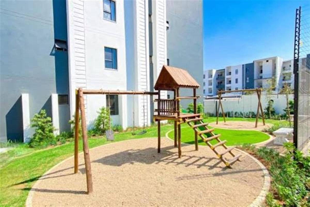 Communal outdoor area featuring a children's playground with wooden climbing frame and swings, set within a landscaped garden space at the apartment complex.
