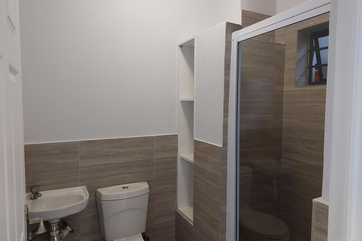 A clean, modern bathroom featuring a wall-mounted basin, toilet, and a glass-enclosed shower with neutral-toned wall tiling and built-in shelving.