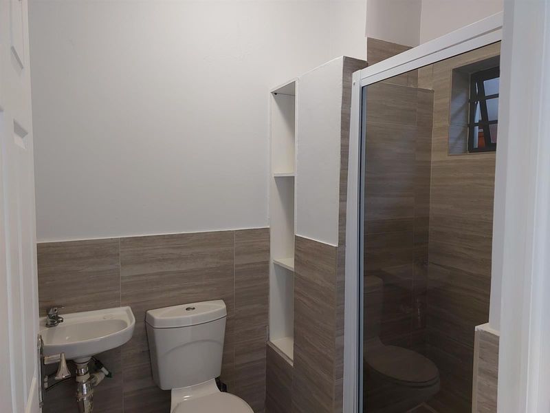 A clean, modern bathroom featuring a wall-mounted basin, toilet, and a glass-enclosed shower with neutral-toned wall tiling and built-in shelving.