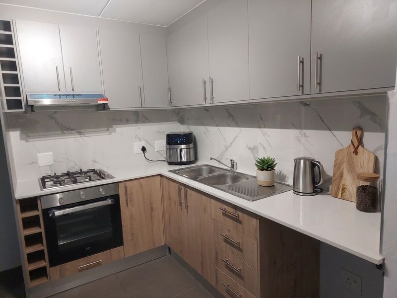 Modern kitchen featuring light wood and grey cabinetry, quartz countertops, marble-look splashback, gas hob, built-in oven, and a double bowl sink.