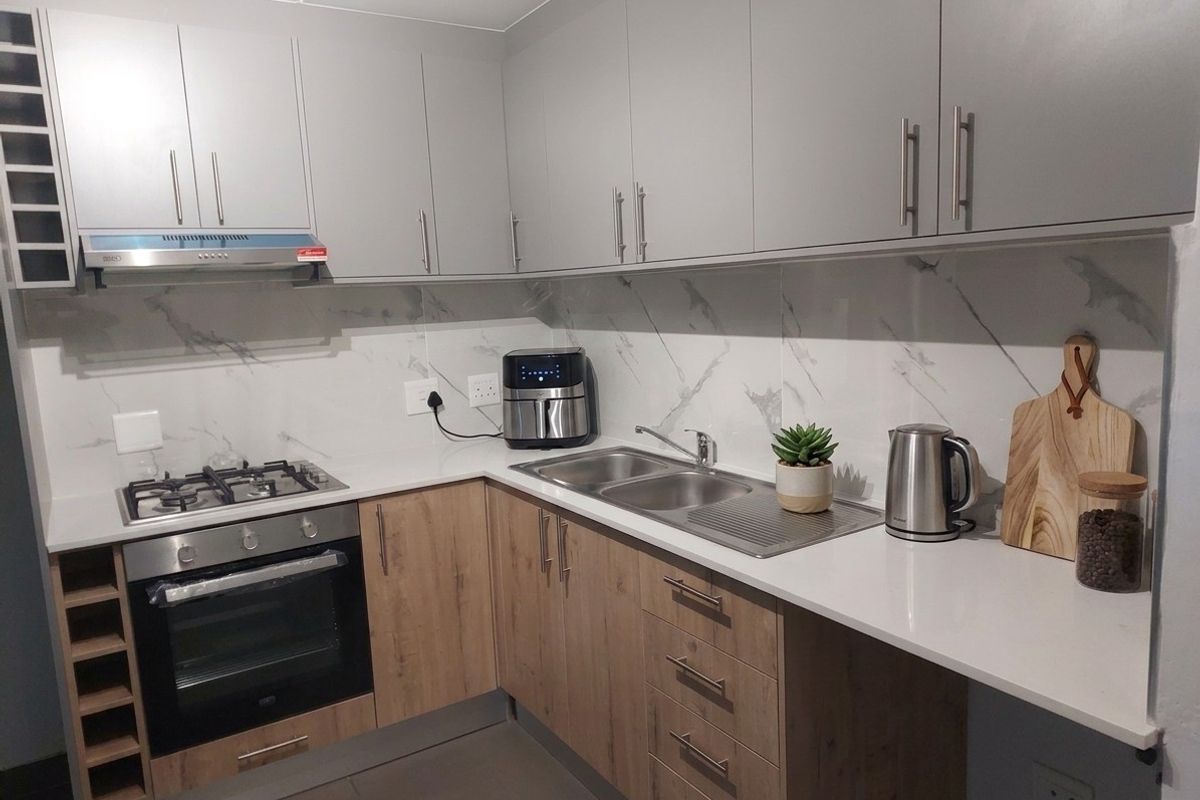 Modern kitchen featuring light wood and grey cabinetry, quartz countertops, marble-look splashback, gas hob, built-in oven, and a double bowl sink.