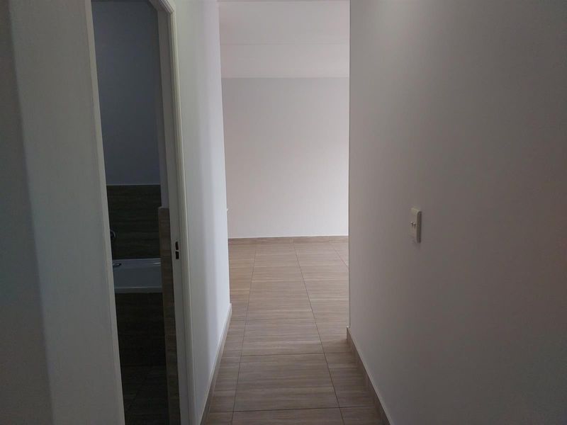 A clean, empty hallway featuring neutral tiled flooring and an archway leading into an adjacent room and bathroom area.