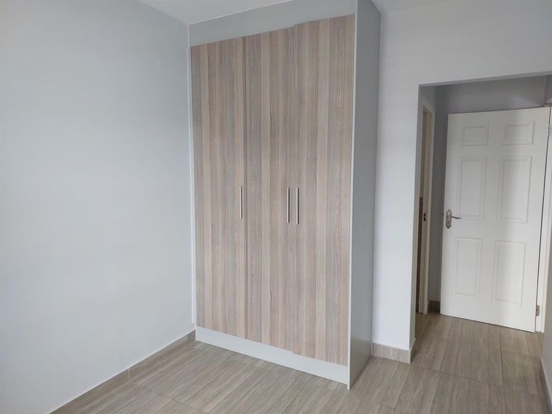 A clean, empty bedroom featuring modern wood-finish built-in wardrobes and neutral tiled flooring.