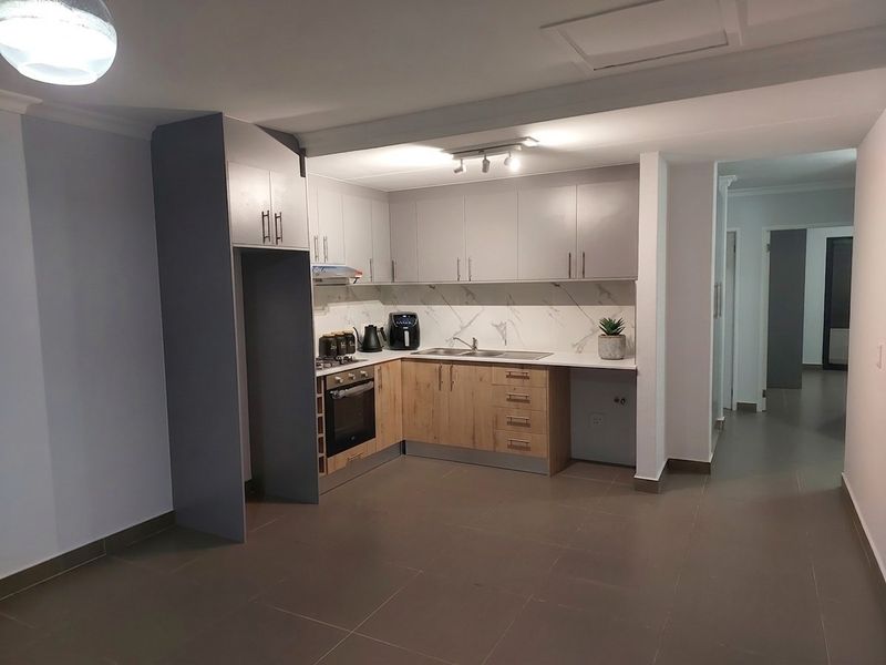 Modern kitchen featuring two-tone cabinetry, marble-look splashback, built-in oven, hob, and extractor fan, set within an open-plan living space with tiled flooring.