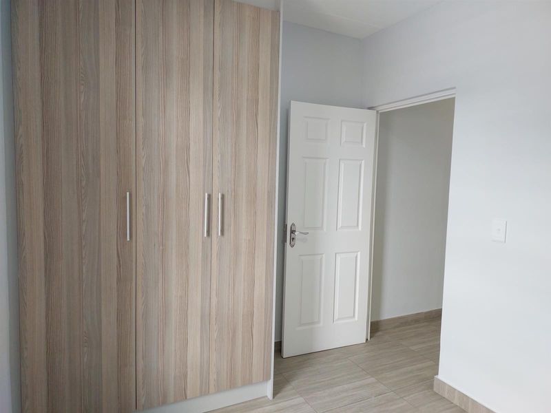 A clean, empty bedroom featuring modern wood-look built-in cupboards, neutral tiled flooring, and a white interior door.