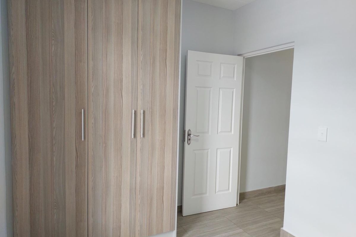 A clean, empty bedroom featuring modern wood-look built-in cupboards, neutral tiled flooring, and a white interior door.