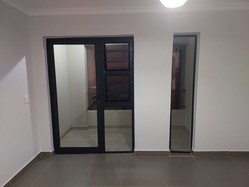An empty living area featuring modern tiled flooring, neutral walls, and aluminium framed glass doors leading to an outdoor space.