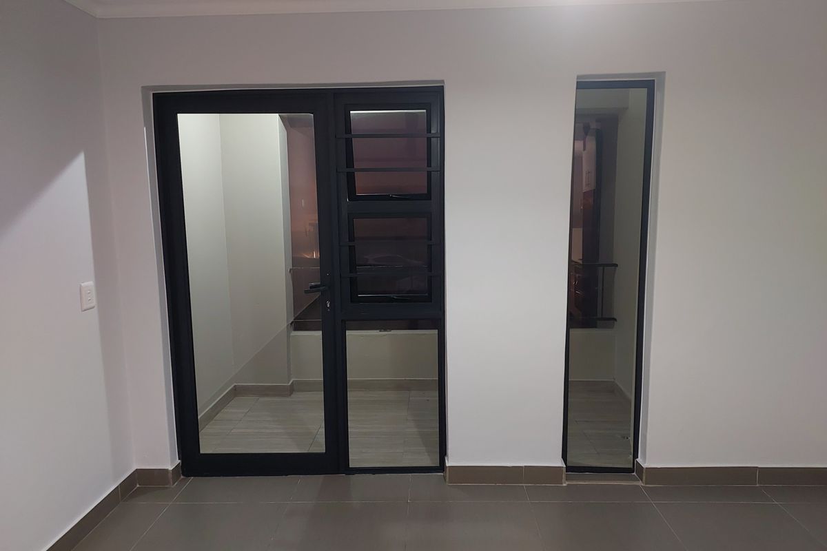 An empty living area featuring modern tiled flooring, neutral walls, and aluminium framed glass doors leading to an outdoor space.