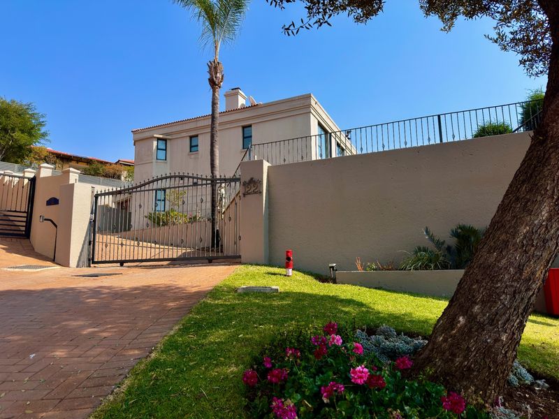 Front elevation of a multi-story residence featuring a paved driveway, secure wrought iron gate, and well-maintained boundary wall with landscaped garden.