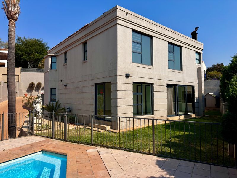 Rear view of a two-story residential property featuring a swimming pool, paved deck, metal fencing, and modern aluminium-framed windows and sliding doors.