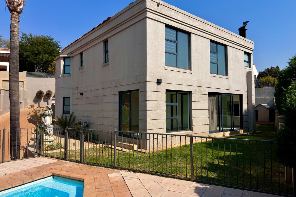 Rear view of a two-story residential property featuring a swimming pool, paved deck, metal fencing, and modern aluminium-framed windows and sliding doors.